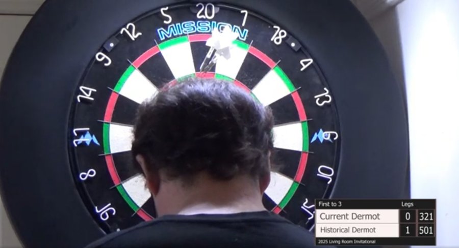 A shot of the back of my head, bowed, as I fiddle with my scoring app. I am standing in front of a dartboard, above my head you can see three darts nestled neatly in the T20 bed.